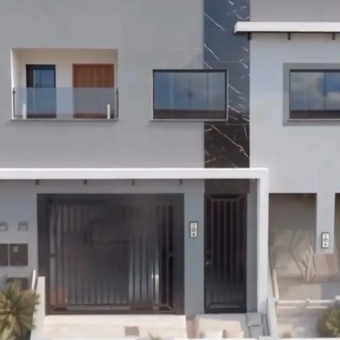 Casas geminadas de dois andares, fachada cinza com revestimento escuro, portões pretos e varandas com guarda-corpo de vidro